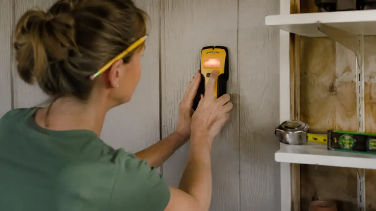 Close-up of a stud finder being run along a shed wall before mounting a tool rack